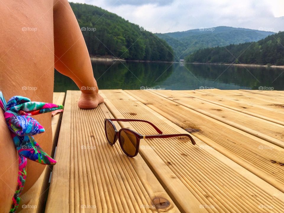 Woman's tanned legs on wooden pontoon with sunglasses near