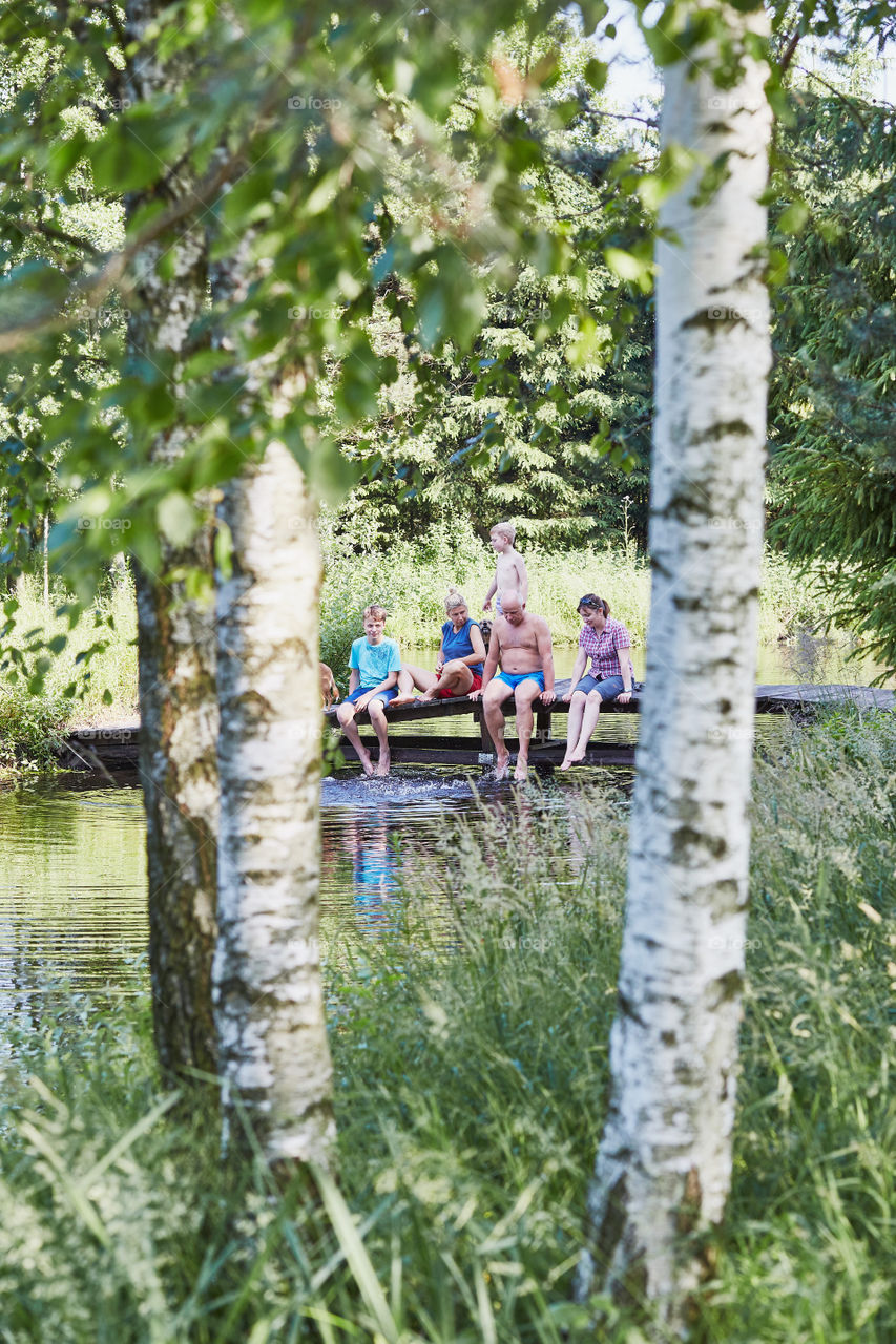 Family spending time together sitting on a bridge over a lake, among the trees, close to nature, during summer vacations. Candid people, real moments, authentic situations