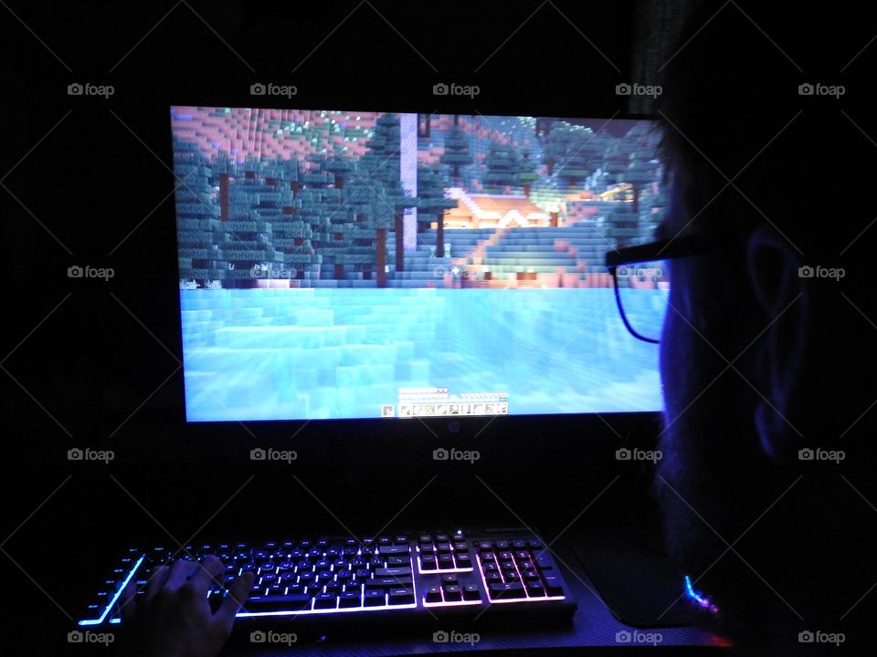 Teenager boy playing Minecraft on the gaming computer seen from his glasses close-up in a dark room.