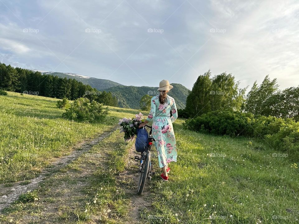 Girl in a dress with lilacs on a bicycle