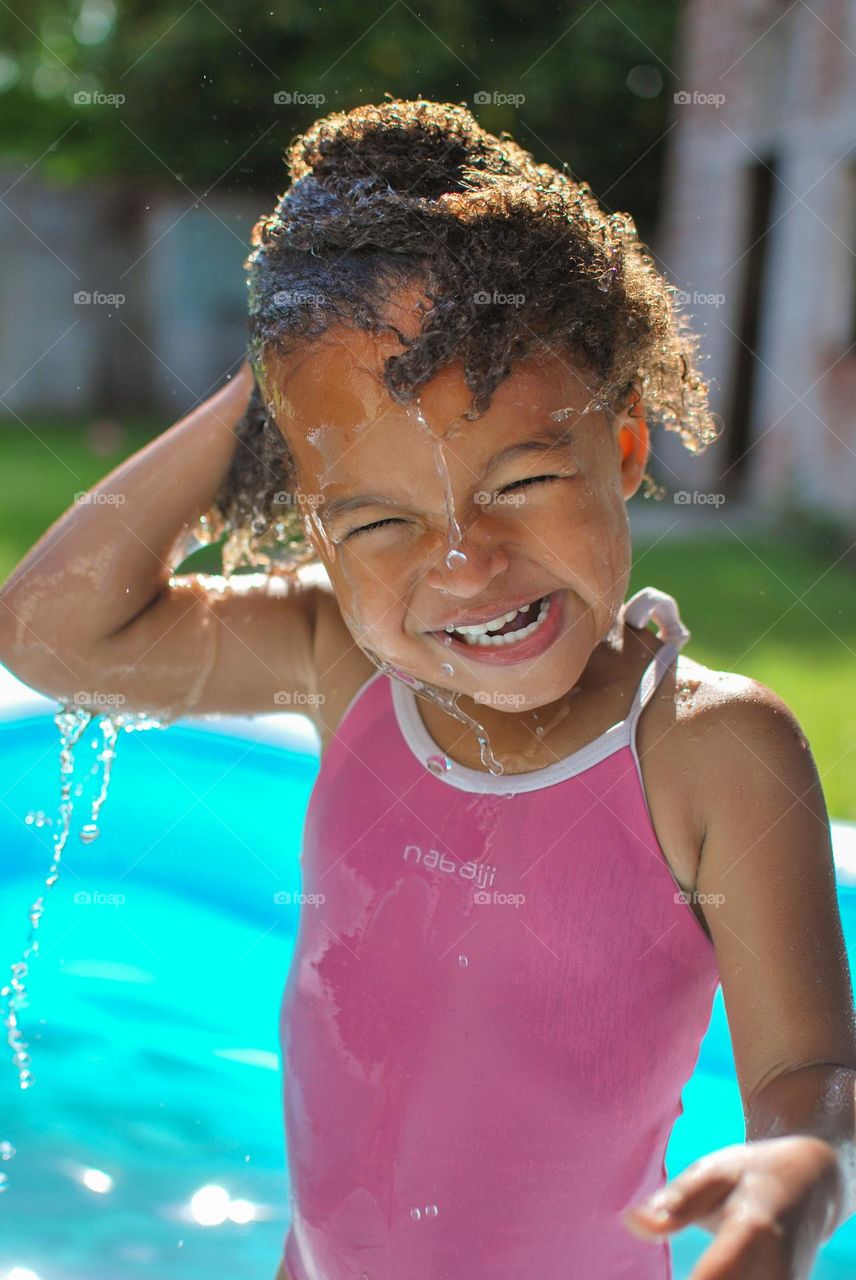 Girl of mixed race enjoying the refreshment of water in a swimming pool on a hot summer day (family, fun, summer, water, blue, swimming suit, splash, hot, enjoy, play, outdoors