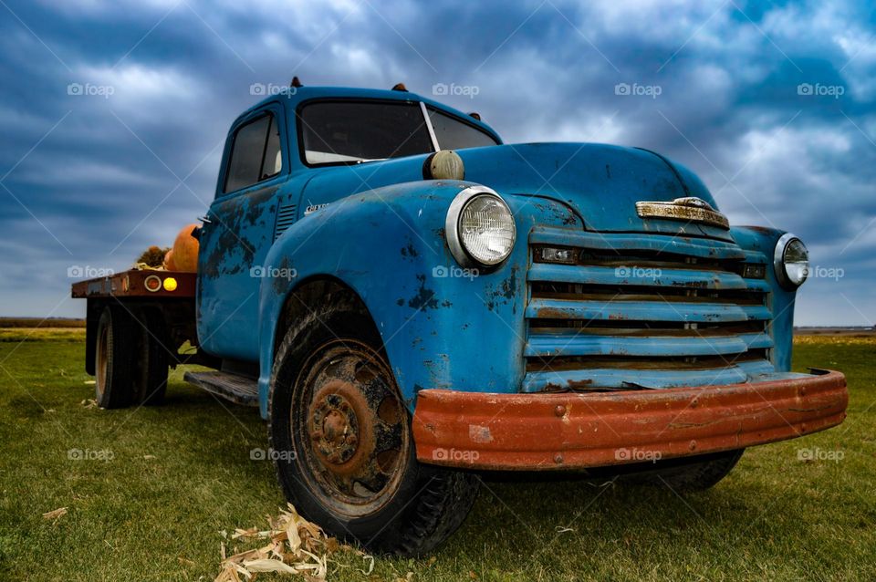a vintage cobalt flatbed pick-up truck against a stormy sky