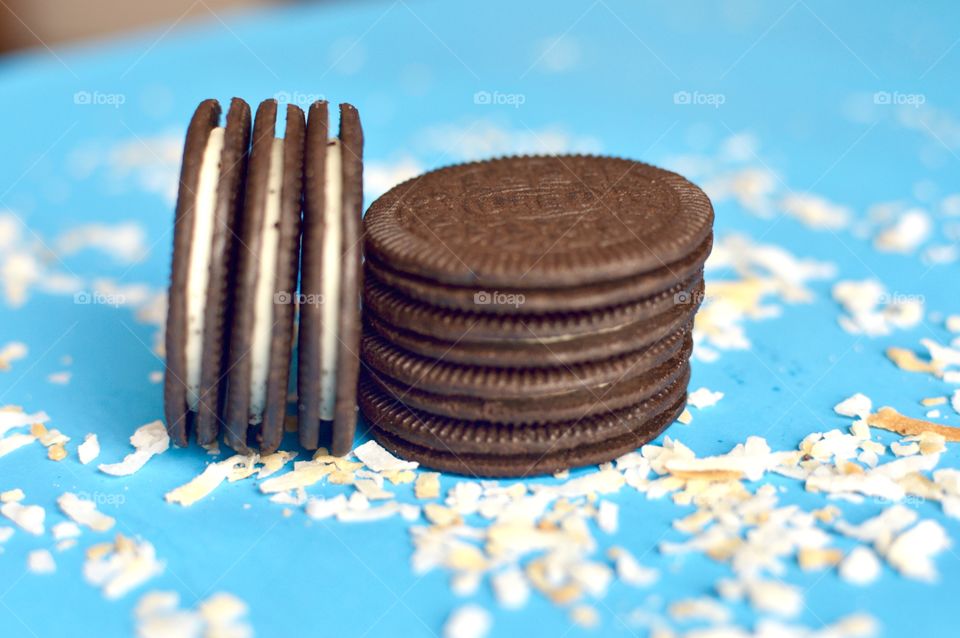 A stack of coconut Oreo thin cookies on a blue background with coconut shreds