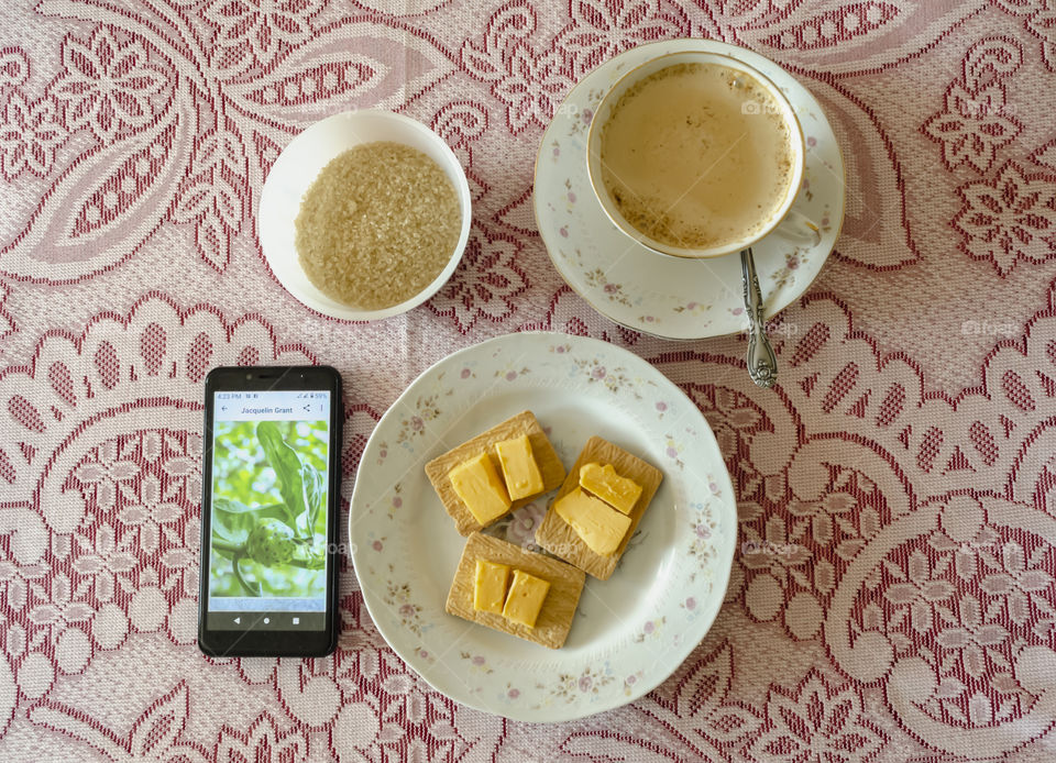 A Layout Of A Cup Of Hot Coffee, Sugar, Biscuit And Cheese And A Mobile Phone