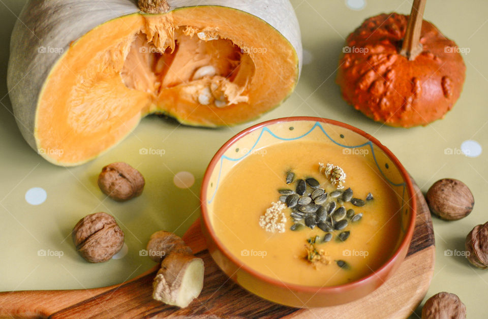 Autumn mood at home. Pumpkin soup with ginger, seeds, walnuts on cutting board and pumpkins on the table.