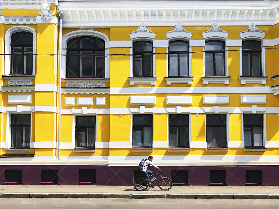 Young man riding a bicycle and using mobile phone in front of an old yellow building in the city 
