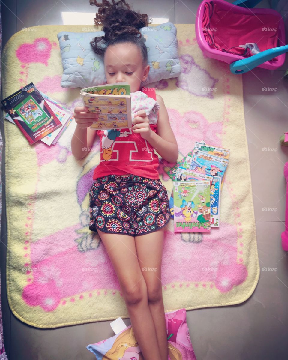 Little girl lying on the bedroom floor reading comic books