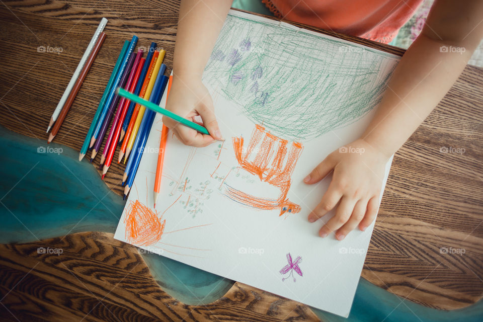 Little girl drawing with colorful pencils at wooden desk indoor