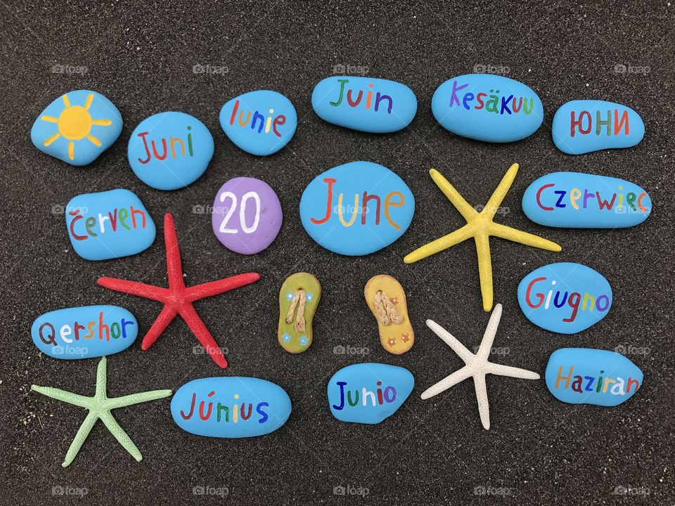 20 June, calendar date with multicolored stones and starfishes over black volcanic sand