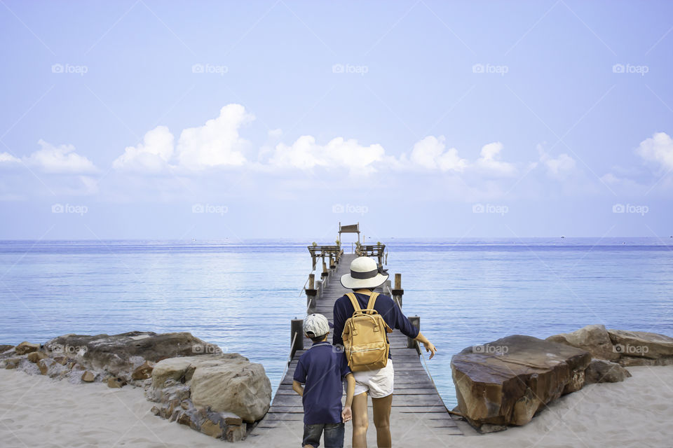 Mother and son walking on wooden bridge pier boat in the sea and the bright sky at Koh Kood, Trat in Thailand.