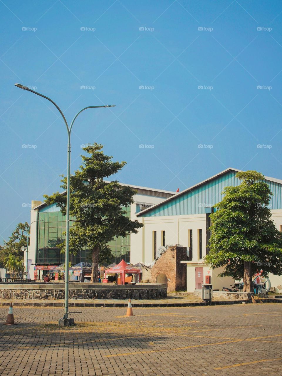 Long distance view of buildings with modern and traditional architecture, a tree, and street lights under a bright blue sky