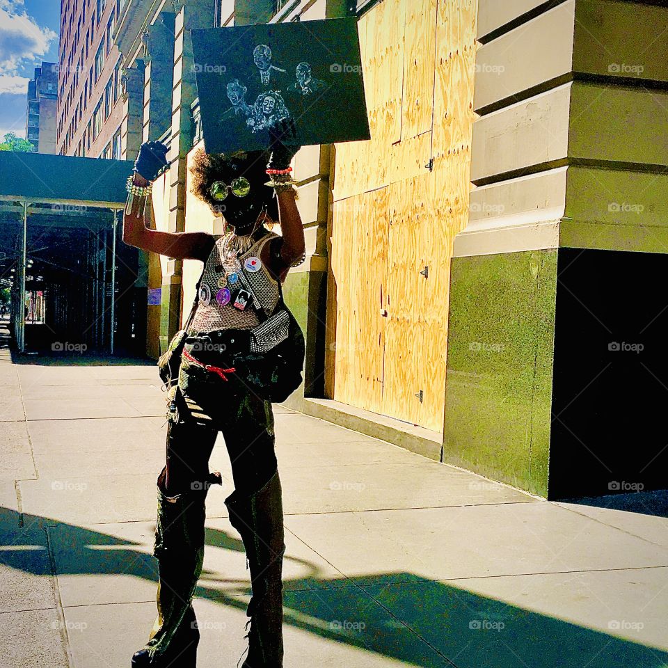 A street artist in blackface wearing mirror lens sunglasses and holding up a sign encountered one summer evening in New York’s West Village on 14th Street in 2020. Hypnotic Productions