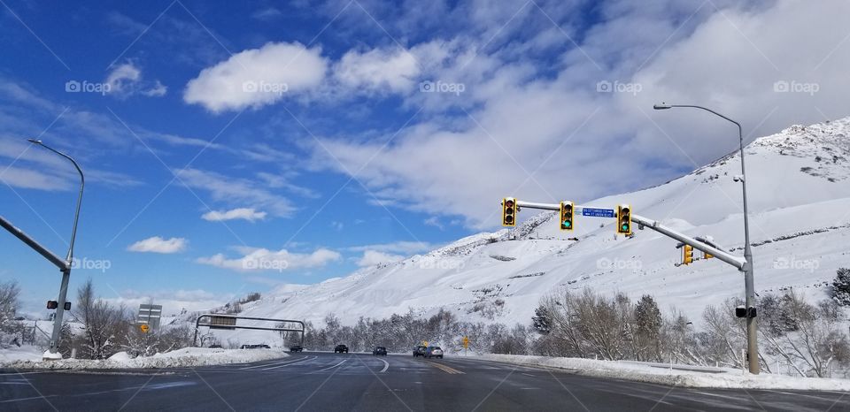 #winter here we have beautiful 💙blue  skies with white clouds floating by. There are tall mountains with snow all around. lights and a road down below.