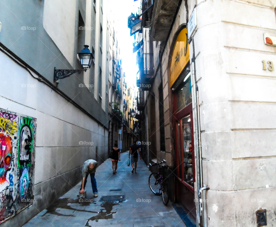 A shop owner washes the alleyway as people shop in the gothic quarter Barcelona Spain