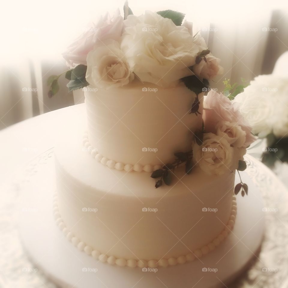 Beautiful white wedding cake with roses and icing pearls on a round table