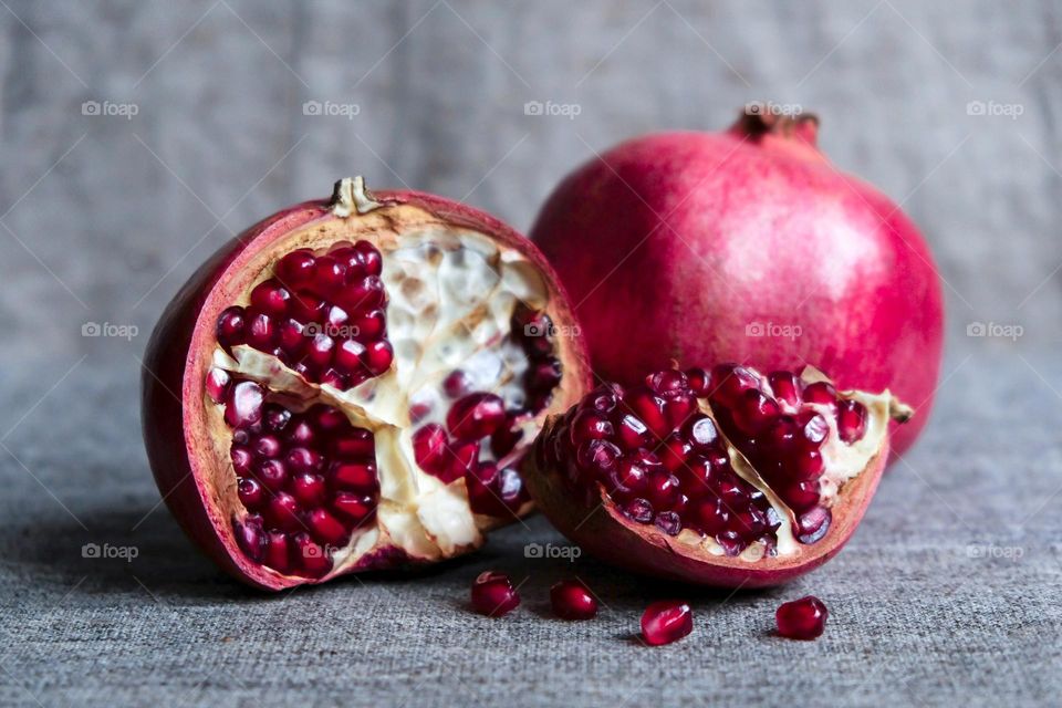 Still life with whole and cut magenta pomegranates on a gray cloth