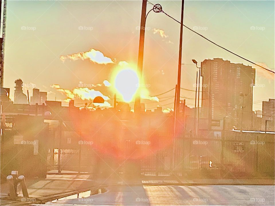 A bright setting sun bathes everything in its golden glow as it makes its way to setting behind the horizon at Newtown Creek in Long Island City, Queens, NY. 2021. Hypnotic Productions