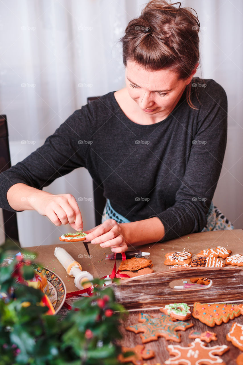 Woman decorating baked Christmas gingerbread cookies with frosting
