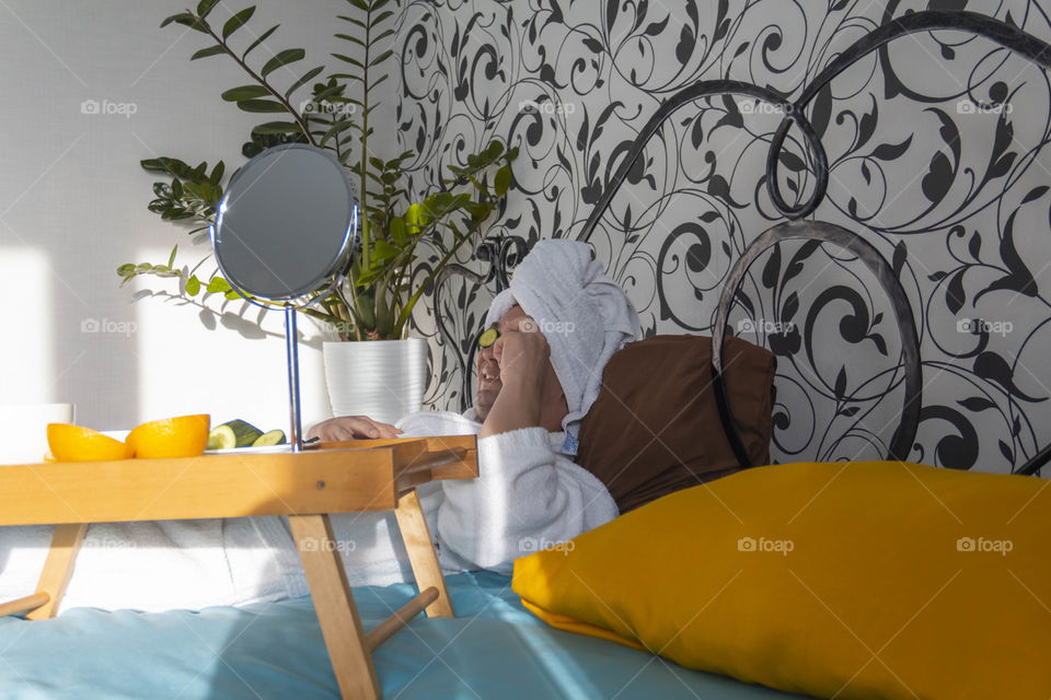 A man and home spa care at home takes care of himself and smears his face with cream, does a manicure at home on a blue background and with oranges and rests.