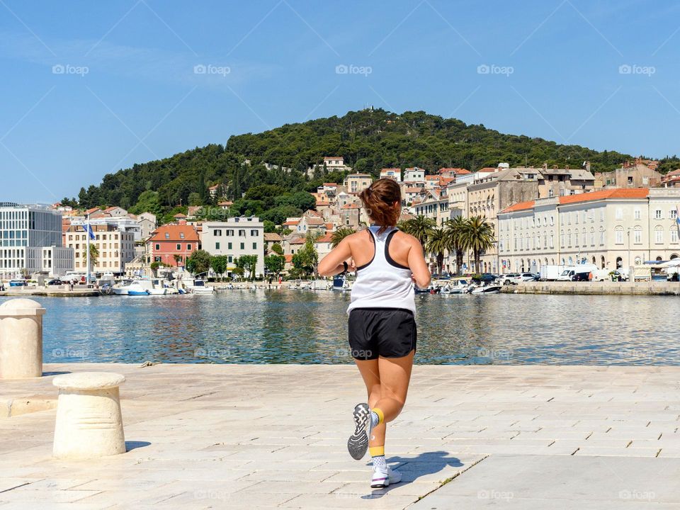 Rear view of female running on shore in city on a sunny day in summer