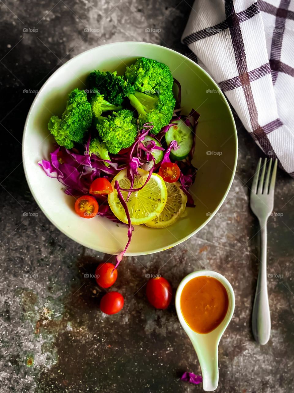 Steamed broccoli and some cherry tomatoes and purple cabbage and slices of lemon in a bowl