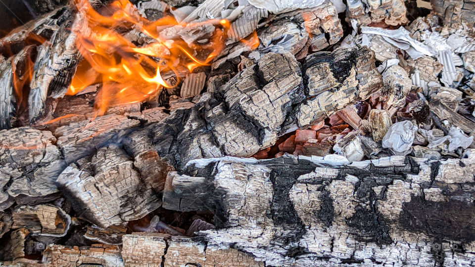 Fire wood, coal and amber ash closeup. Red tongues of flame and glowing amber.