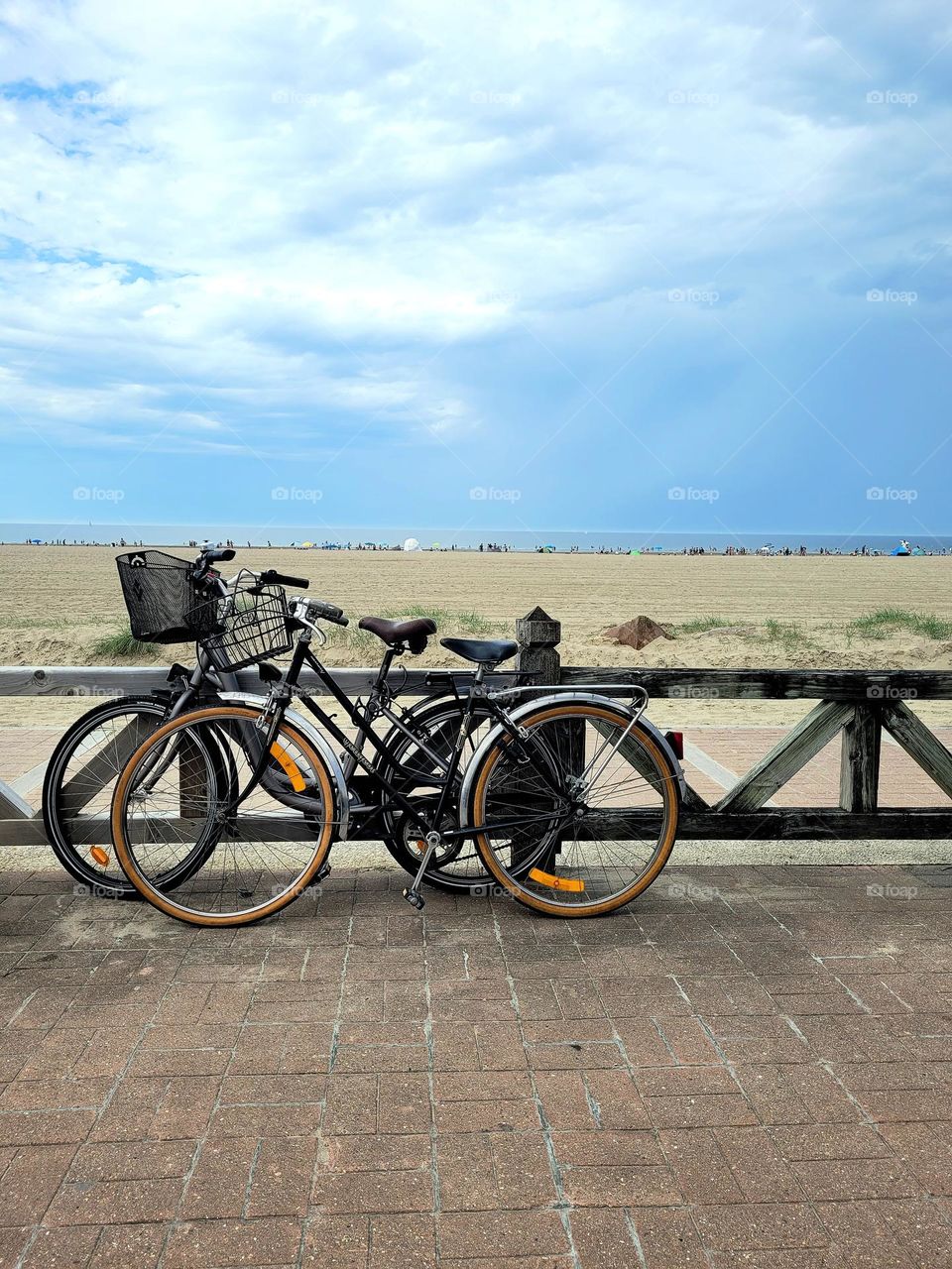 Two bikes parked along a beach in cloudy weather.