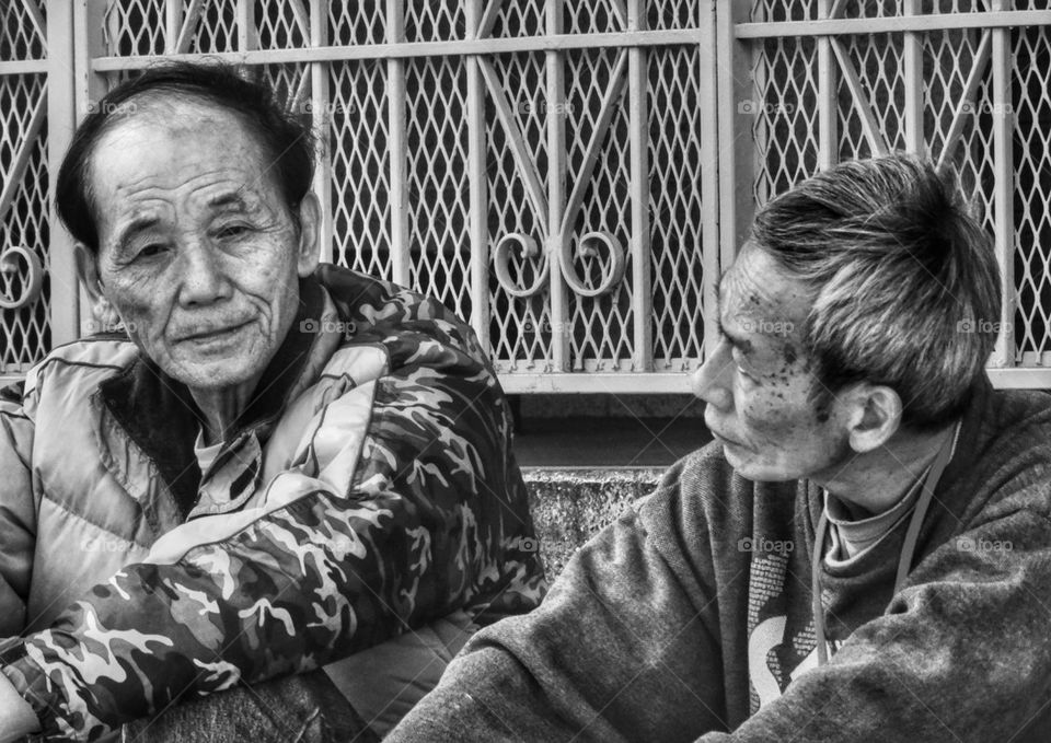 Two Old Asian Men Chat On A Doorstep. Old Men Deep In Conversation
