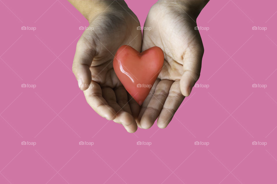 Hand holding a red candy shape heart on a pink background with clipping path for Valentine Day.