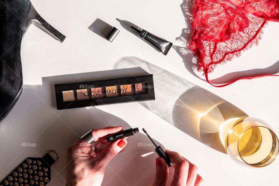 Overhead hard light shot of cosmetics on a table and a woman’s hands holding mascara 