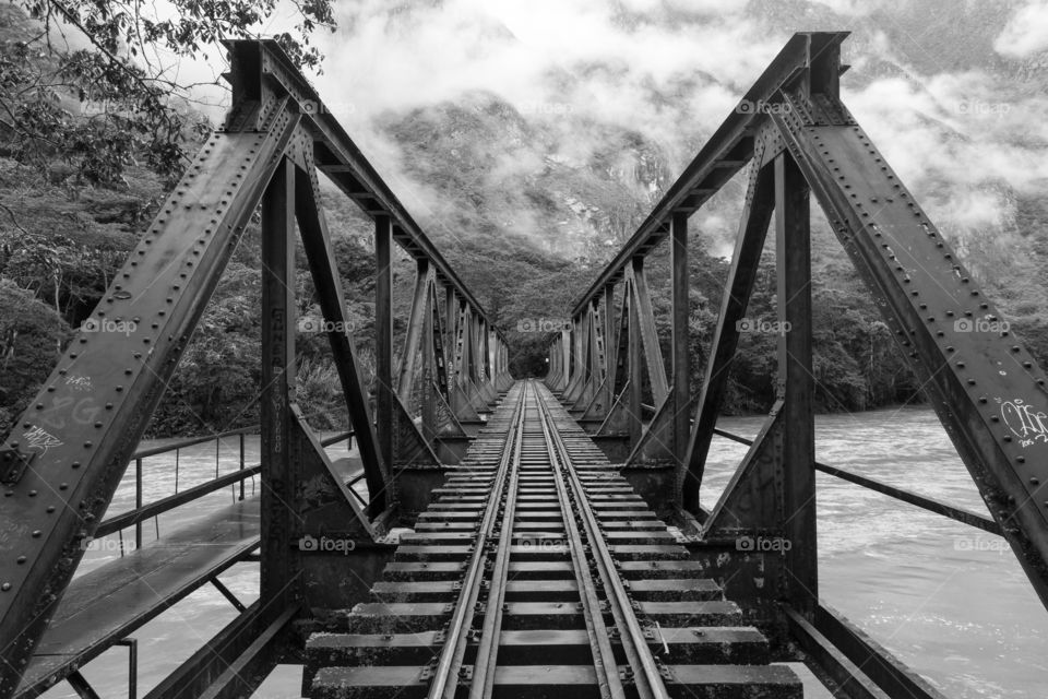 Railroad bridge over river. Metal railroad bridge over wide river. Railroad tracks disappear to horizon. Misty mountains in the background