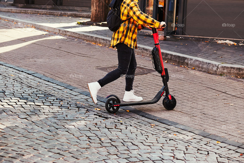 Girl using electric scooter in the street in downtown rented by using service on smartphone. Candid people, real moments, authentic situations