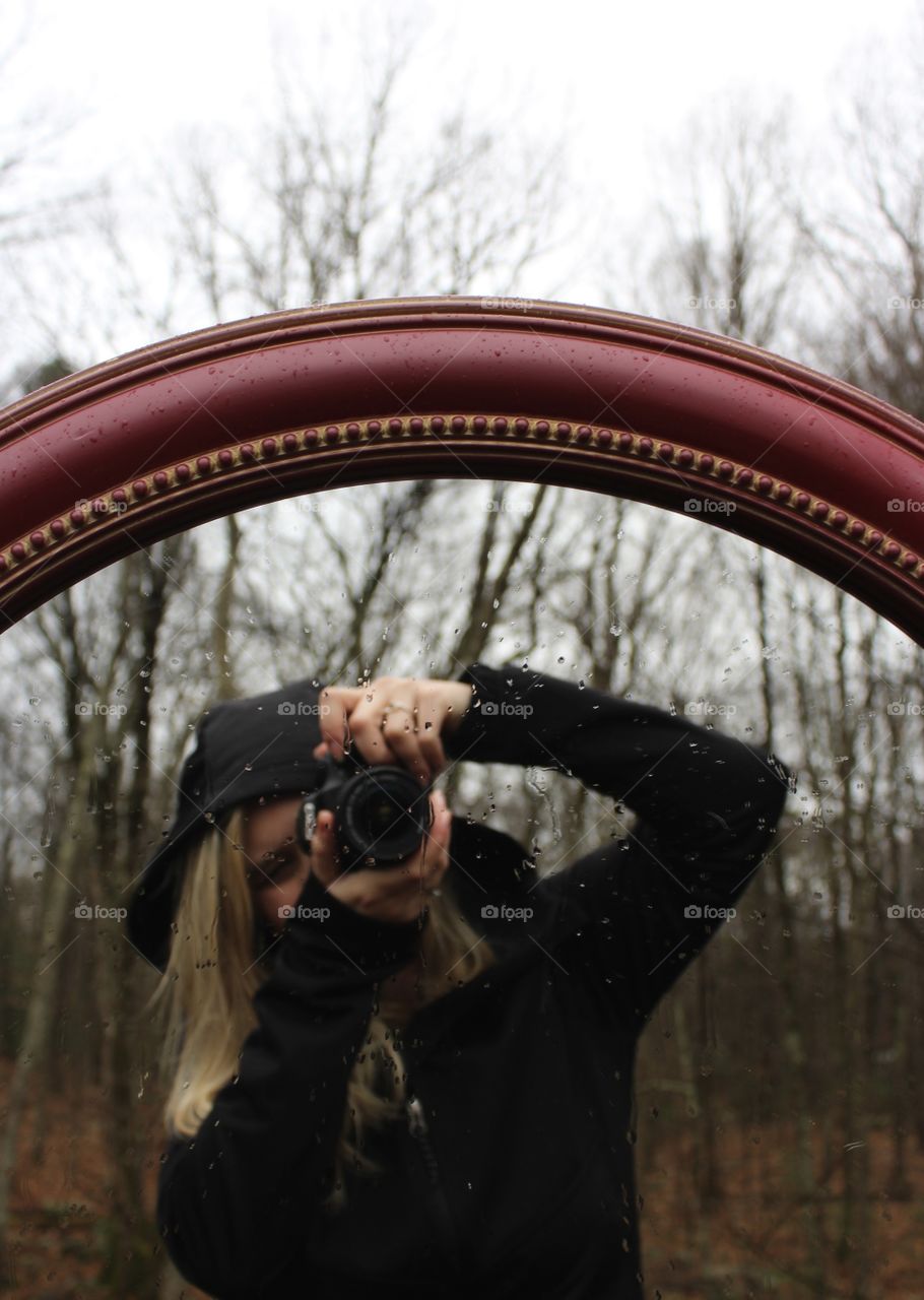 Outdoor Reflection; Woman taking a photo of herself through a mirror outdoors in the rain 