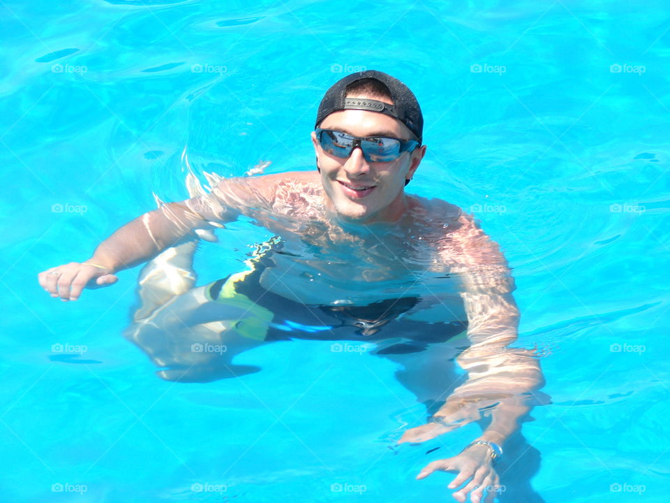 Young man swimming in pool wearing sunglasses