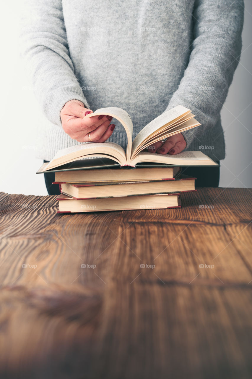 Young woman turning pages of old book on wooden table in antique bookstore. Woman wearing grey sweater and jeans. Vertical photo. Space for text