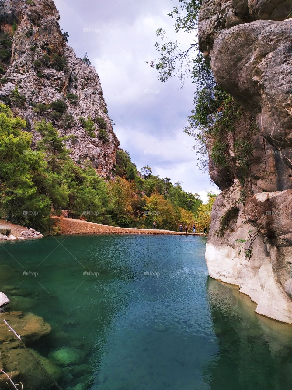 Beautiful lake with rock wall, mountain, nature, trees and small people.