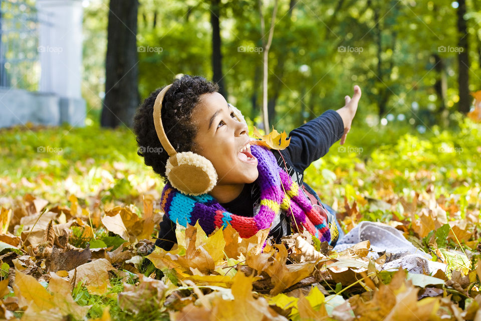 Little boy playing in pile of autumn leaves