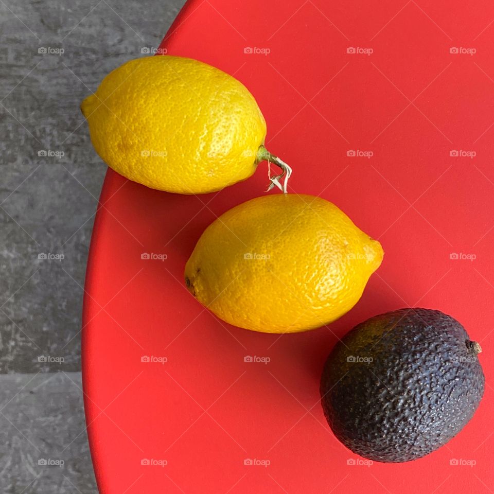 Two lemons and an avocado on a red table 