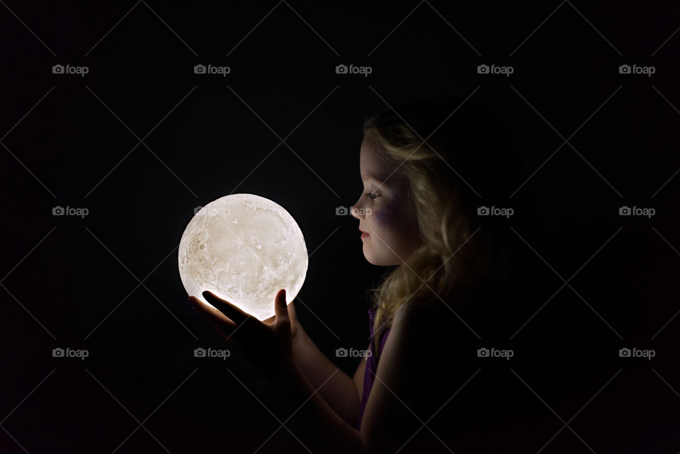 Little girl holding the moon in her hands profile
