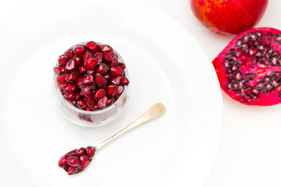 Fresh! Clean simple image with bowl and spoon with pomegranate seeds and fresh cut pomegranate on the side. White background