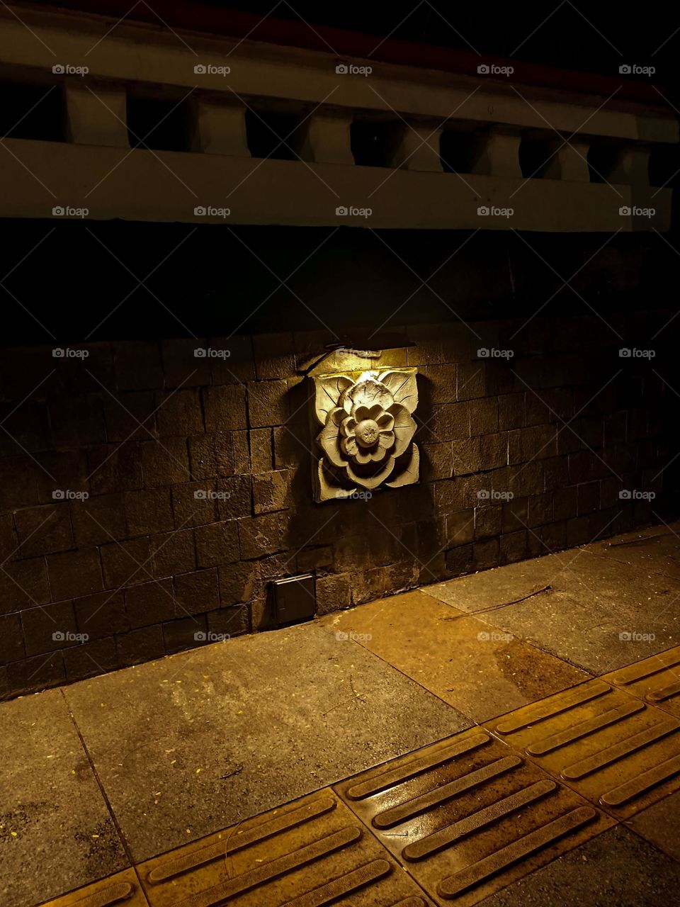 Close-up of a floral ornament illuminated from behind, providing a dramatic effect against the surrounding dark brick wall and concrete floor