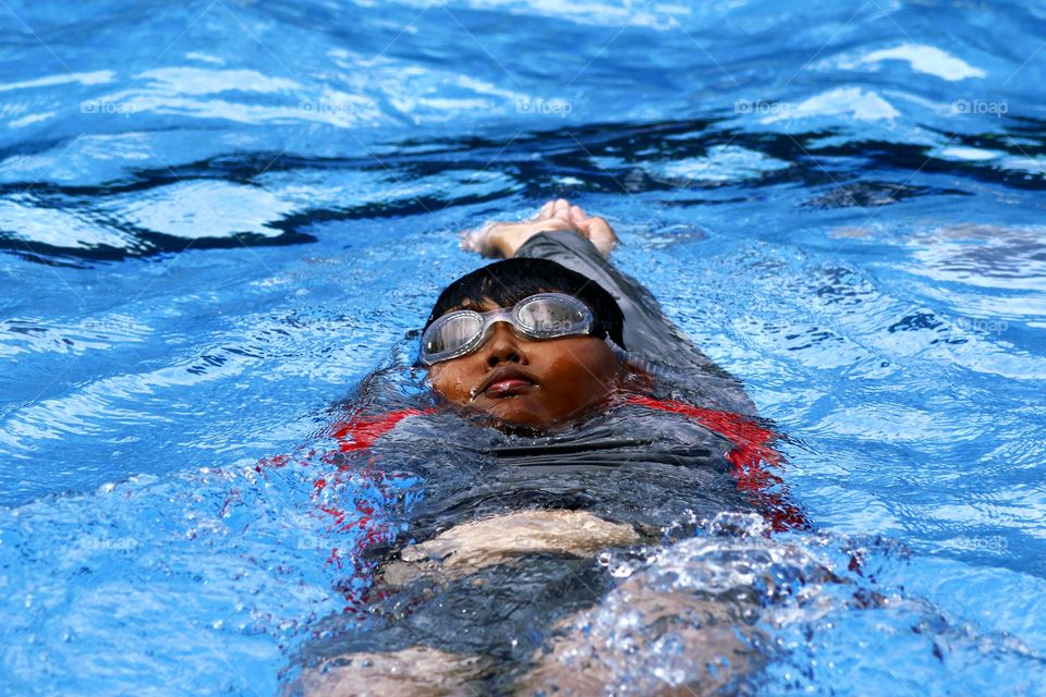 a young boy doing the swimming back stroke in a pool