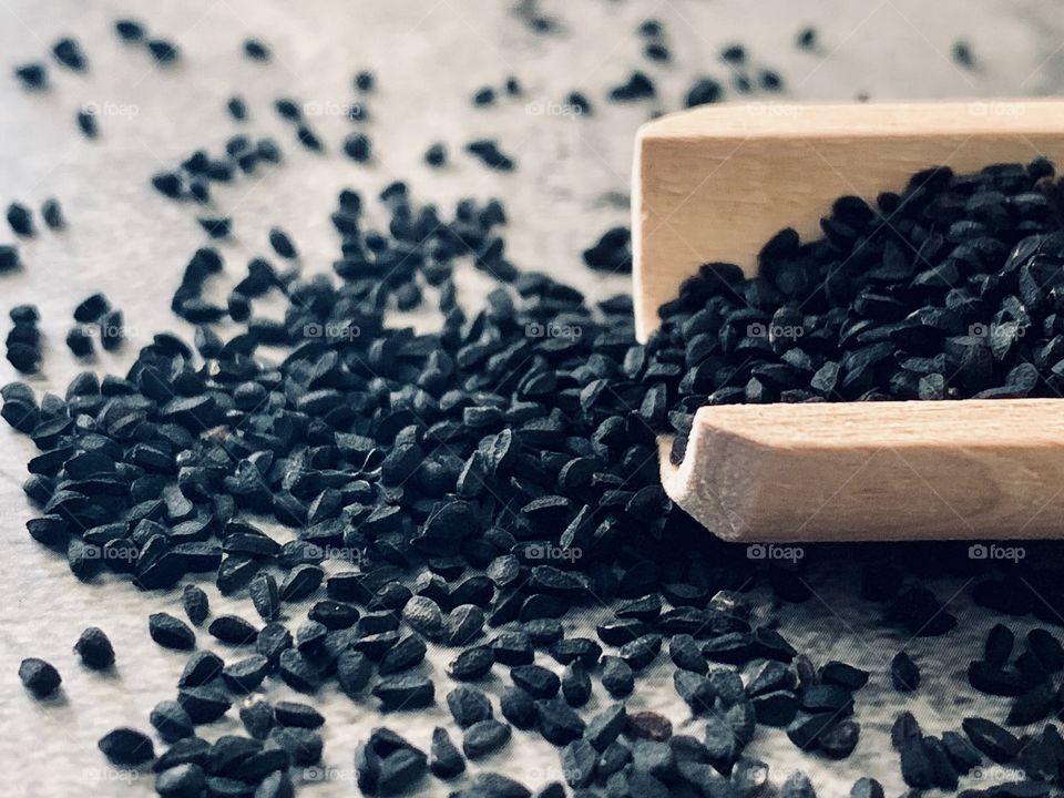 Closeup of black seed spilling out of a wooden scoop on stone surface 