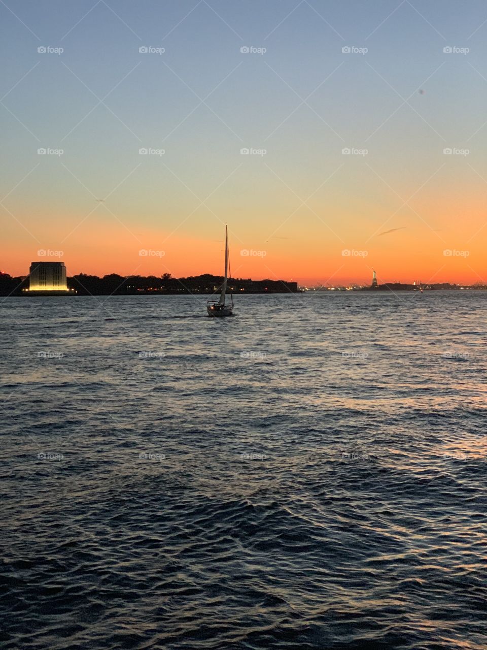 Sail boat drifts into setting sunset. 