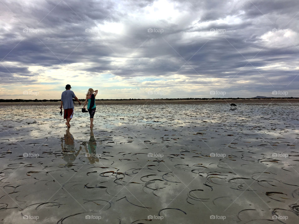 Couple walking on remote secluded beach at low tide late in the day 