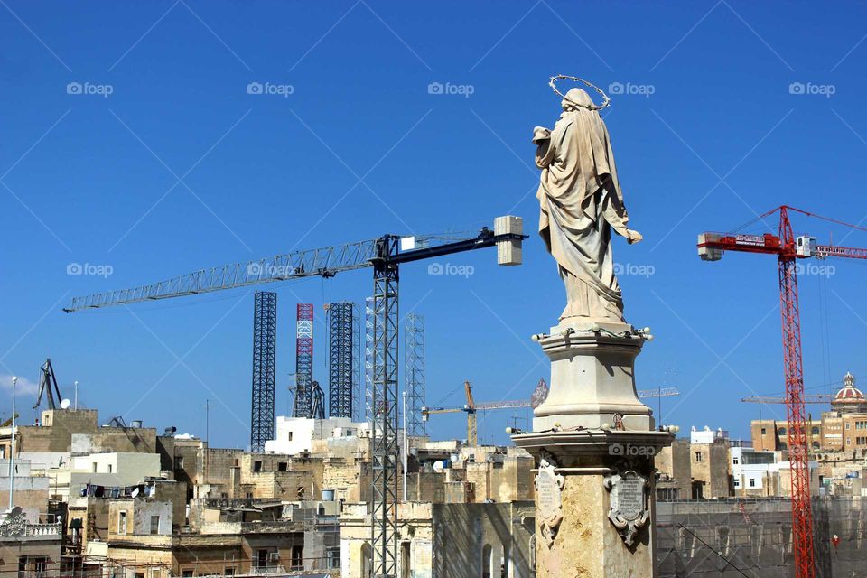 faith and progress. Statue of Virgin Mary between construction cranes