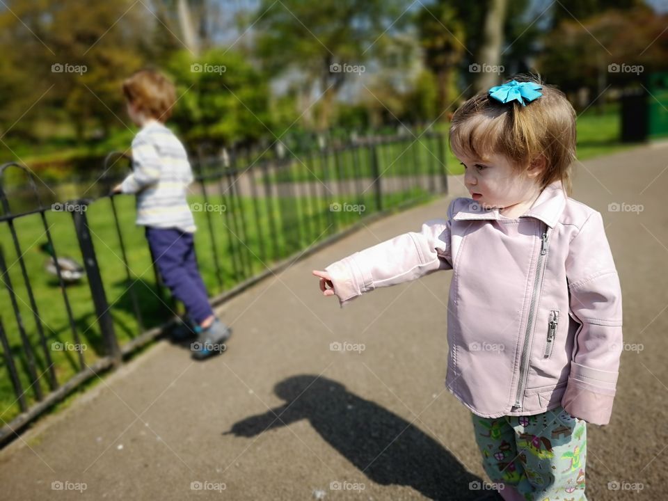 young girl in pink coat and hairbow points to ducks at the park.