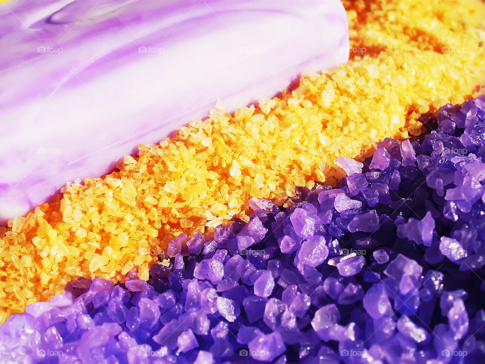 Macro shot of aroma purple and yellow sea salt nearby a lilac bar of soap
