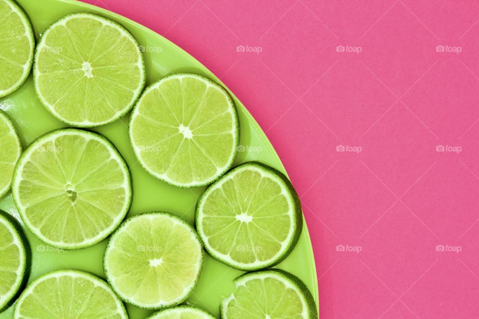 Minimalistic flat lay of lime slices on a green plate against a bright pink background