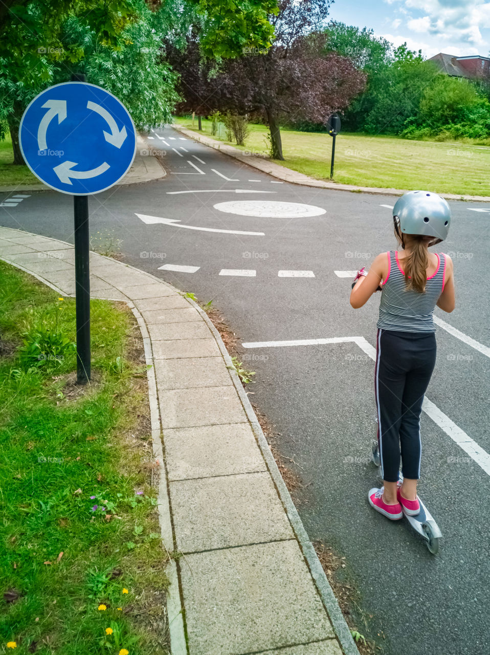 Little girl on scooter approaching roundabout.